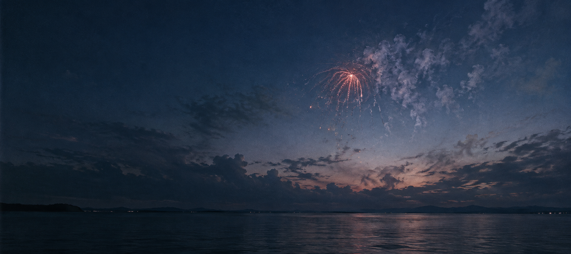 深い蒼の水辺に、消えかけの赤い花火と煙が残る夕景